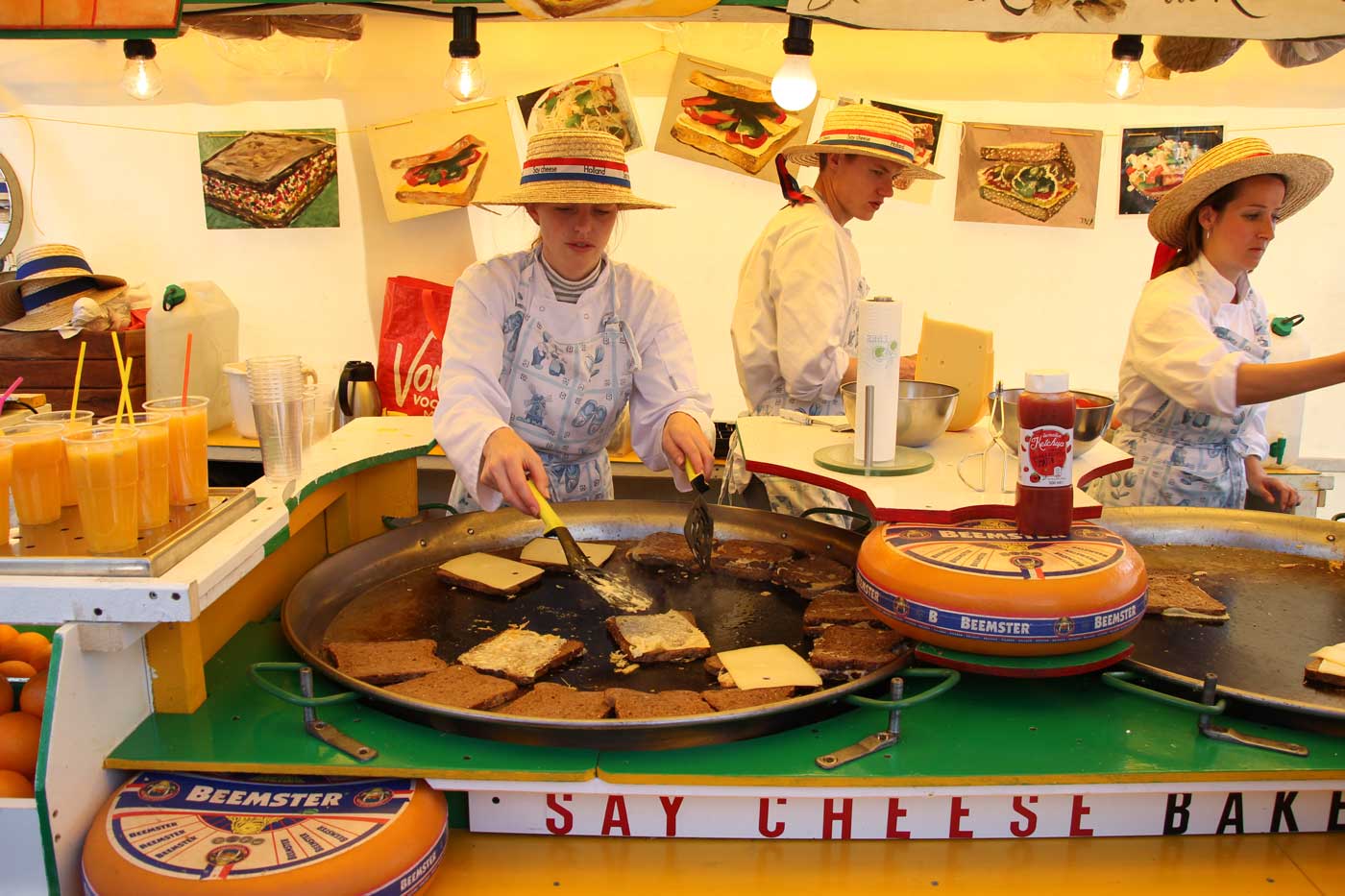 Девушки в канотье предлагают посетителям отведать сыр. На огромной сковороде поджаривают сыр и хлеб.