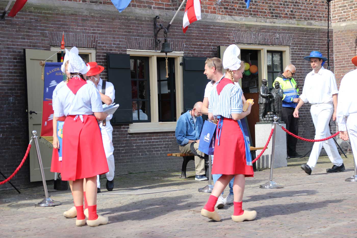 Девушка в традиционном голландском костюме: белом чепчике, полосатой рубашке с коротким рукавом, красной юбке, фартуке и деревянных башмаках-кломпах.