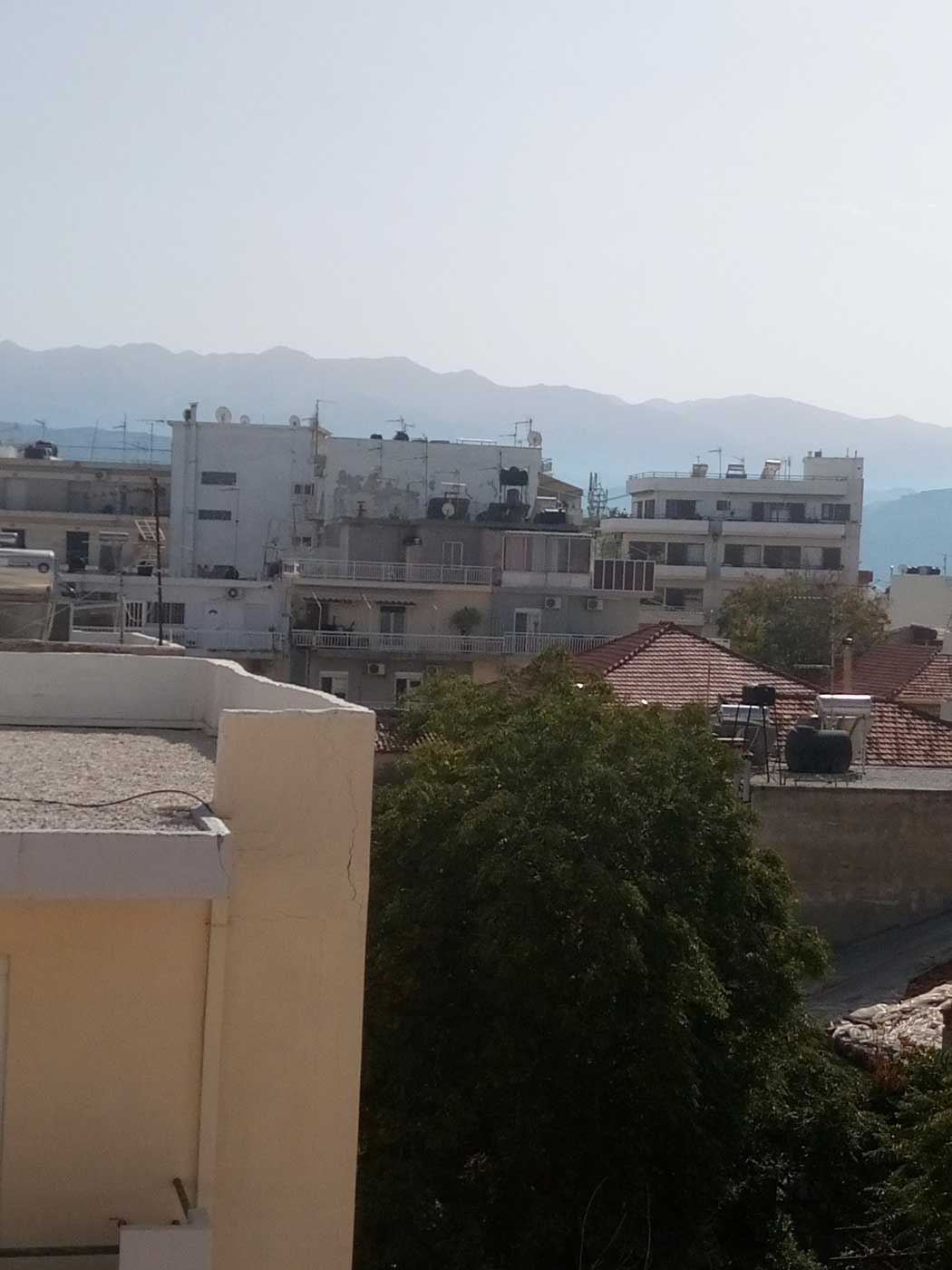 Вид на город из окна. Несколько домов средней высотности, за ними горы.