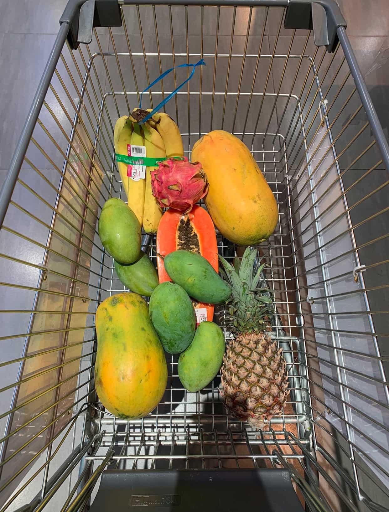 Тележка в супермаркете, в которой лежат экзотические тропические фрукты.