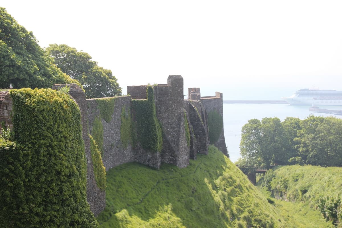 Вид на крепостную стену замка, поросшую мхом. Справа виден пересохший ров, полностью покрытый растительностью.