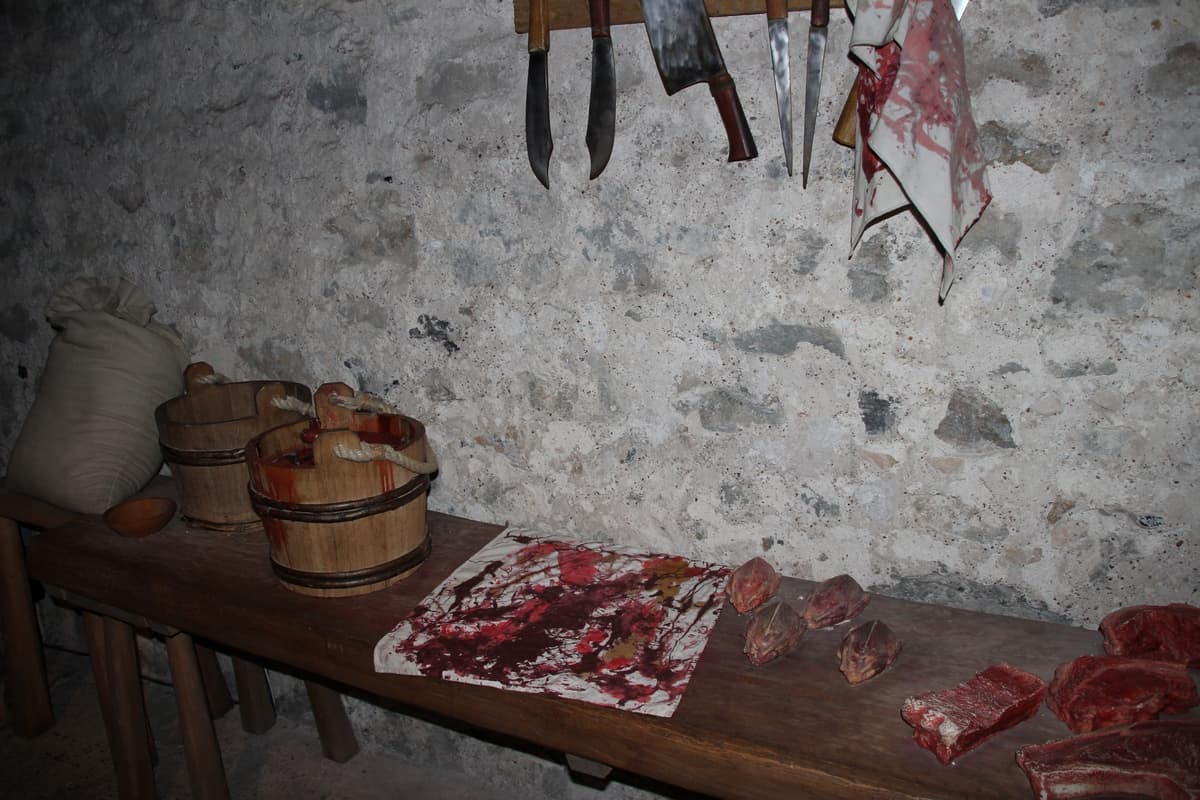 Имитация старинного деревянного стола, на котором лежат куски сырого мяса и деревянные ведра. Над столом висят ножи.